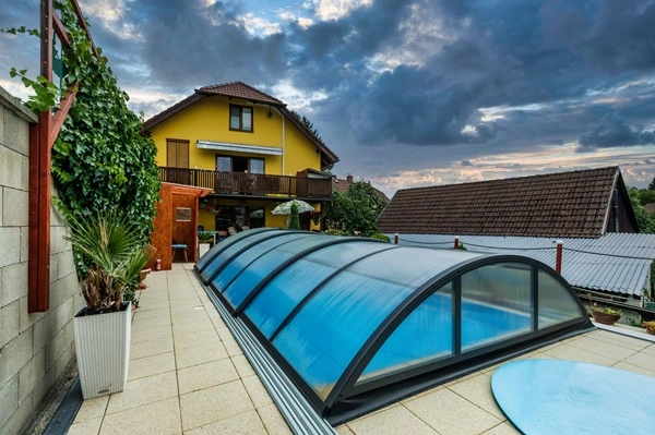 Mittelhohe blaue Poolüberdachung auf einer Terrasse neben einem Wohnhaus